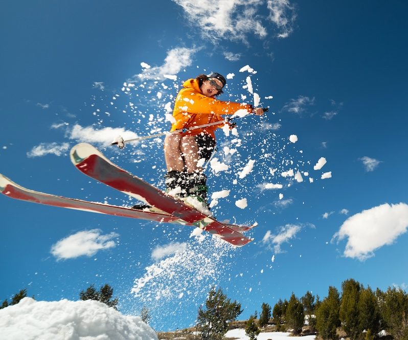 Man skier in flight after jumping from a kicker in the spring against the backdrop of mountains and blue sky. Close-up wide angle. The concept of closing the ski season and skiing in spring.